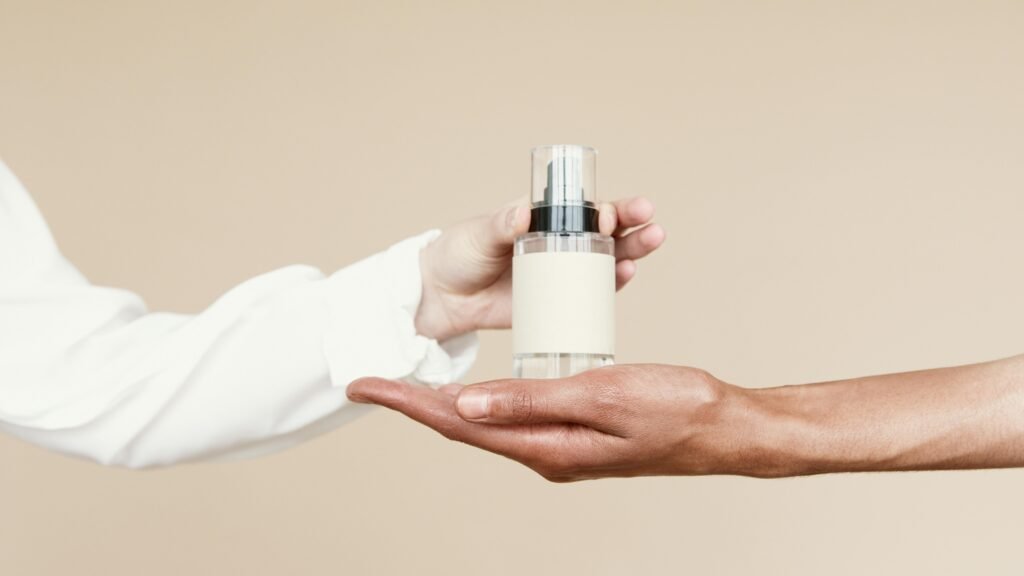Minimalist shot of a perfume bottle being passed between hands against a neutral background.